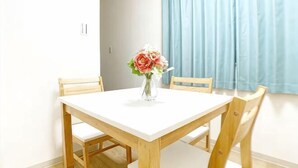 A dining table with chairs, a vase with flowers, and a window with curtains. - SunStay Higashinakano (Tokyo)