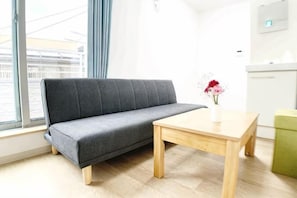 A room with a sofa, a wooden table, a vase with flowers, and a green ottoman.