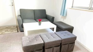 A living area with a grey sofa, a white coffee table, and two grey ottomans. - SunStay Higashinakano (Tokyo)