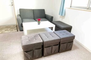 Un espacio de estar con un sofá gris, una mesa de centro blanca y dos otomanas grises.