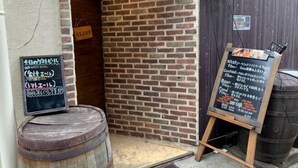 A brick building entrance with a wooden barrel, a chalkboard menu, and a sign indicating a closed area. - SunStay Higashinakano (Tokyo)
