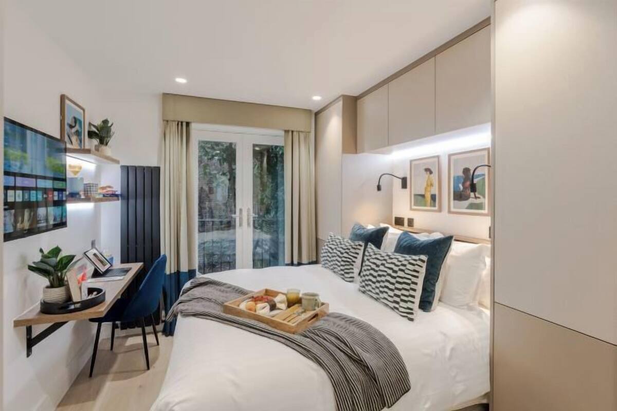 A modern hotel room with a bed, a desk, and a view of the outdoors.