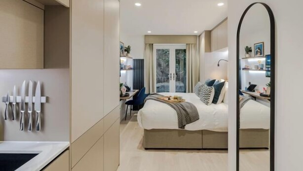A modern hotel room with a bed, bedside table, and a large mirror. - Kensington Deluxe Studio (London)