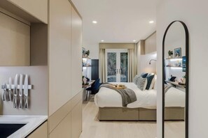 A modern hotel room with a bed, bedside table, and a large mirror. - Kensington Deluxe Studio (London)