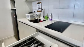 Cocina moderna con placa de inducción negra, armarios blancos, pileta de acero inoxidable y un refrigerador pequeño.