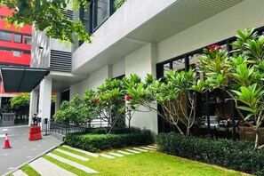 Un edificio moderno con entrada cubierta, césped cuidado y diversas plantas.
