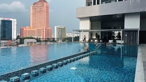 Una piscina con un paisaje urbano al fondo, incluyendo un edificio alto con señalización 'TEO CHEW'.