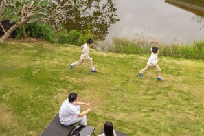 Un espace extérieur verdoyant avec une étendue d’eau, des arbres et une personne assise sur un tapis.