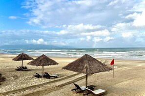 A beach with thatched umbrellas and lounge chairs. - Ocean Villa Da Nang 4BR 5 Beds, Private Pool and Kitchen (Da Nang)