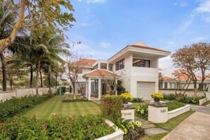 A two-story house with a red-tiled roof, surrounded by a well-maintained garden with various plants and flowers. - Ocean Villa Da Nang 4BR 5 Beds, Private Pool and Kitchen (Da Nang)