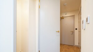 En hall med en vit dörr, trägolv och en klädhängare i bakgrunden.