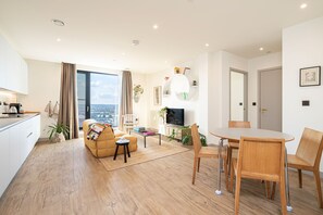 Een moderne woonkamer met een bank, salontafel en eettafel. Er is een televisie, een plant en uitzicht op de stad.