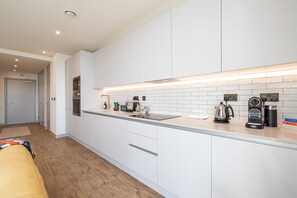 Een moderne keuken met witte kasten, een roestvrijstalen afzuigkap en een aanrecht met waterkoker en koffiezetapparaat.