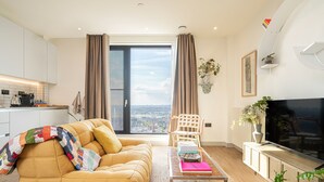 Ein modernes Wohnzimmer mit einer Couch, einem Couchtisch, einem Fernseher und Blick auf die Stadt durch ein großes Fenster.