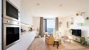Eine moderne Küche mit integrierten Geräten, ein Essbereich mit Sofa und Couchtisch sowie ein Wohnzimmer mit Fernseher und Pflanzen.