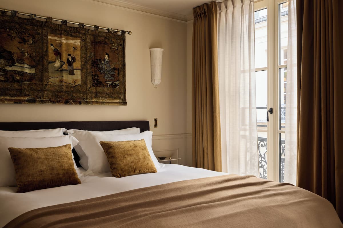 A hotel room with a large bed, a headboard, a wall-mounted artwork, a window with curtains, and a view of the outside.