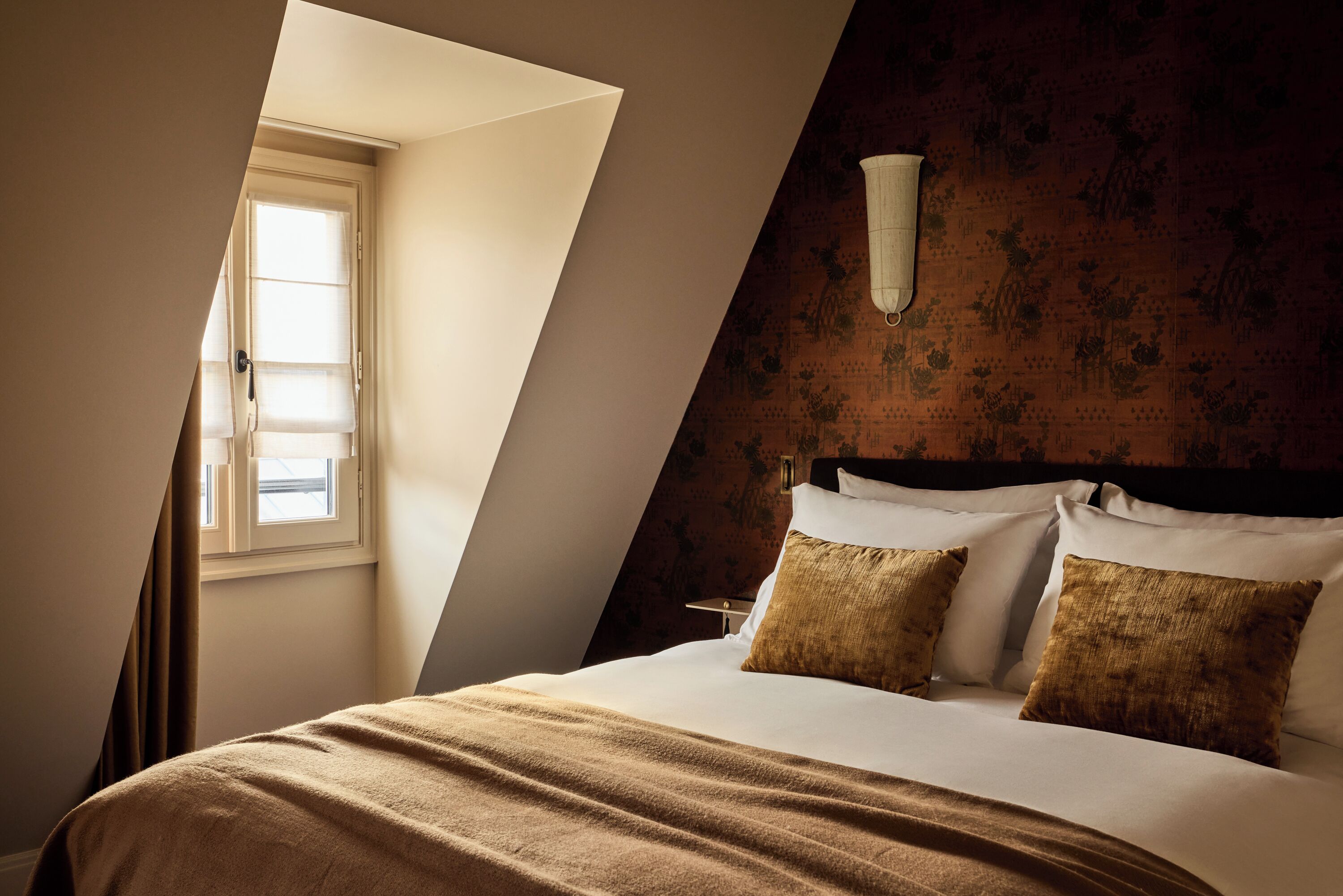 A bedroom with a bed, a window, and a wall with a floral pattern.