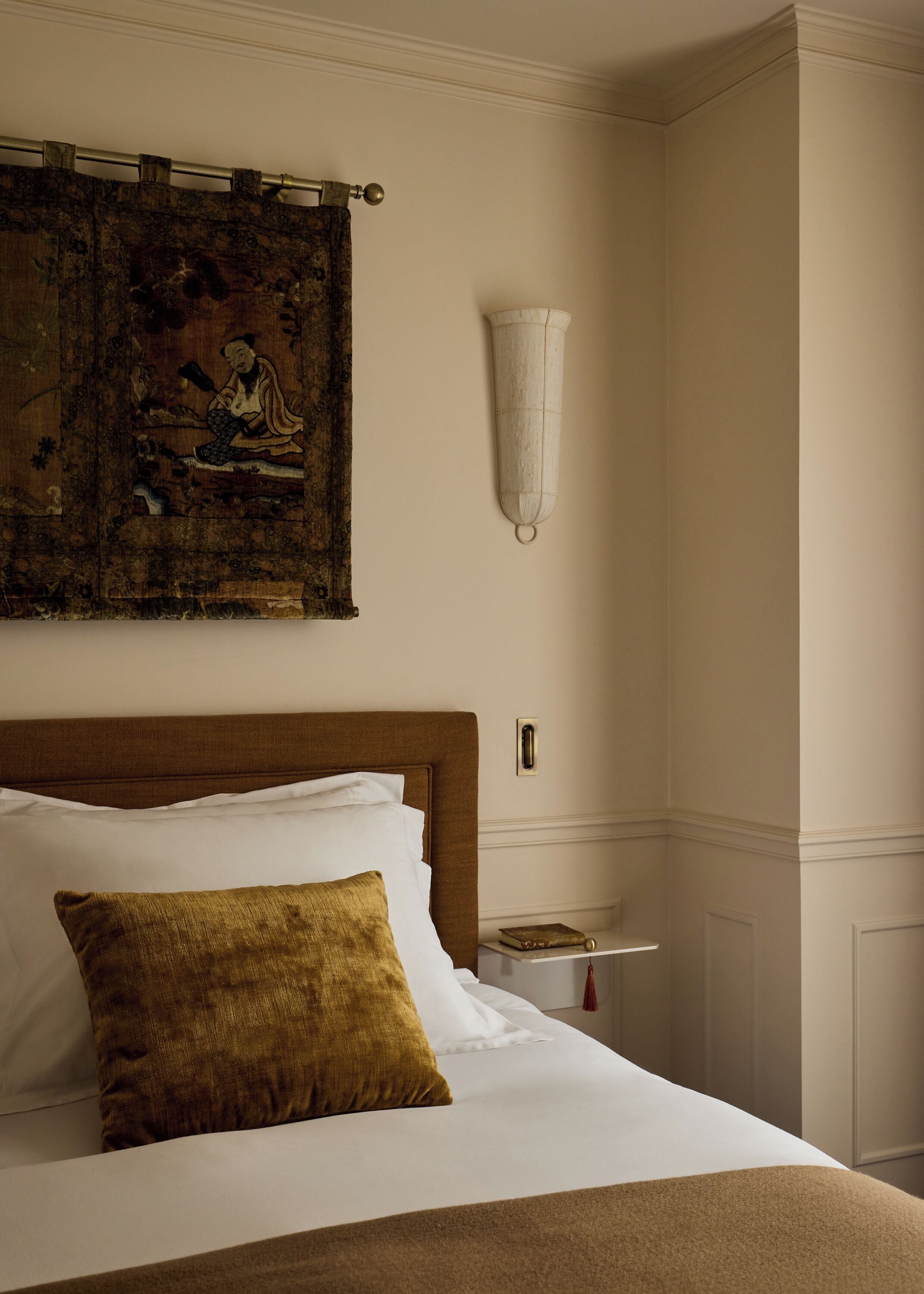 Een netjes opgemaakt bed met wit en bruin beddengoed, een klassiek hoofdbord en een decoratief kussen.
