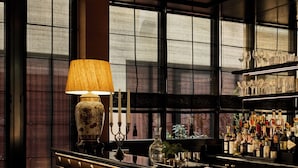 A bar area with a lamp, bottles, and a view through large windows. - L'Opale Noire (Paris)