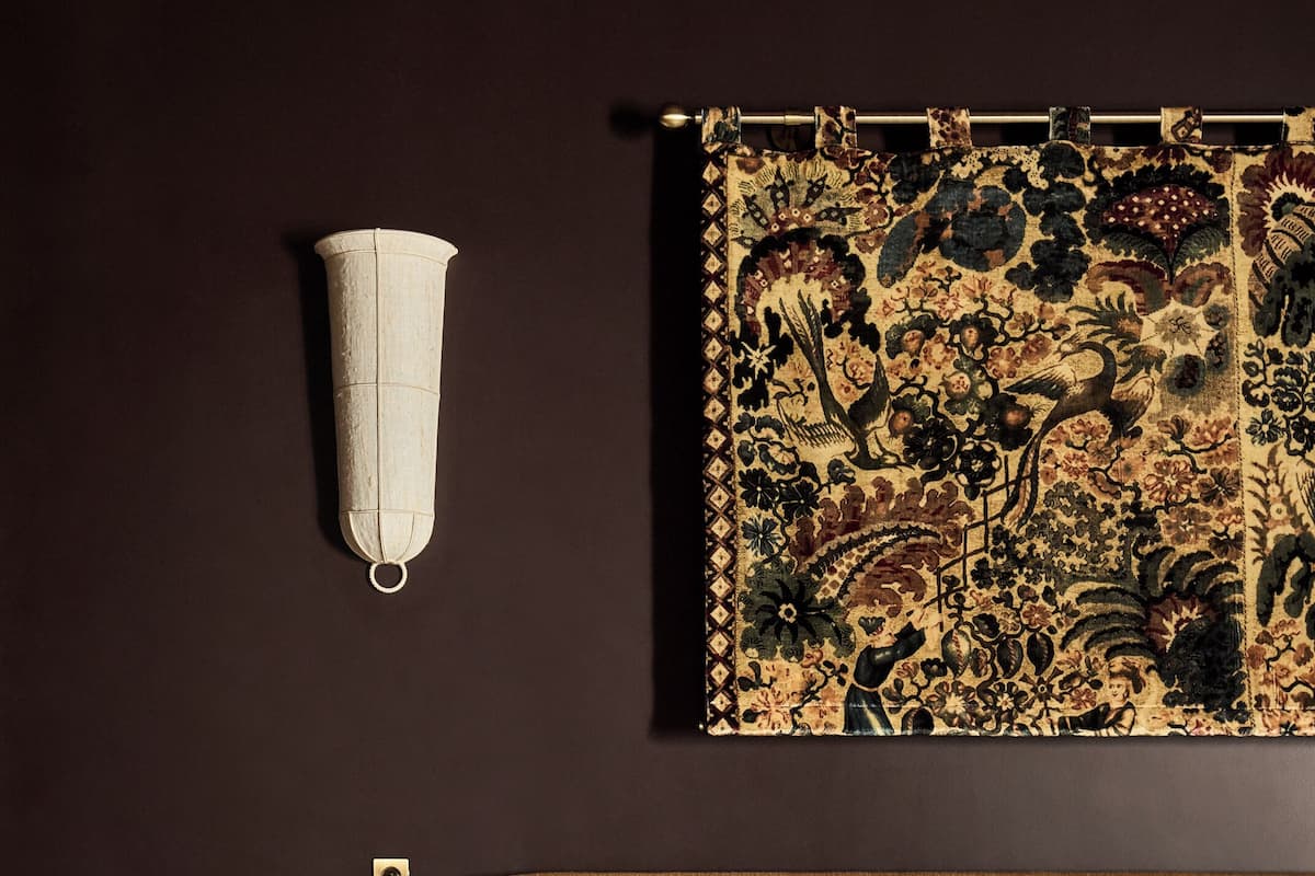 A bedroom with a bed, a wall-mounted lamp, and a tapestry.