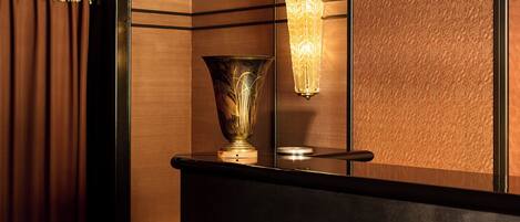 Balcão de madeira escura com um vaso decorativo e luminária fixada na parede.