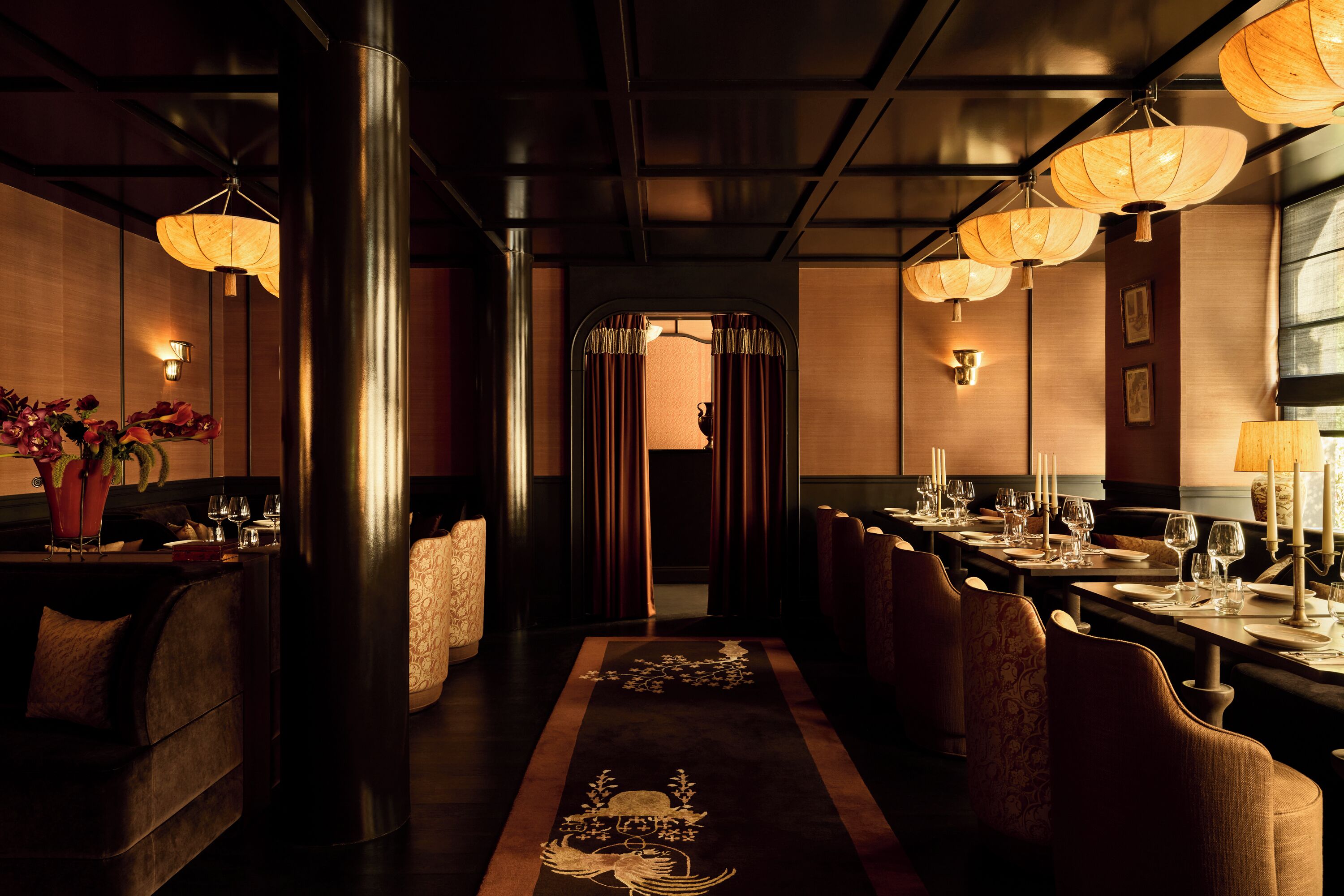 A dimly lit restaurant with a long table, chairs, and hanging lanterns.