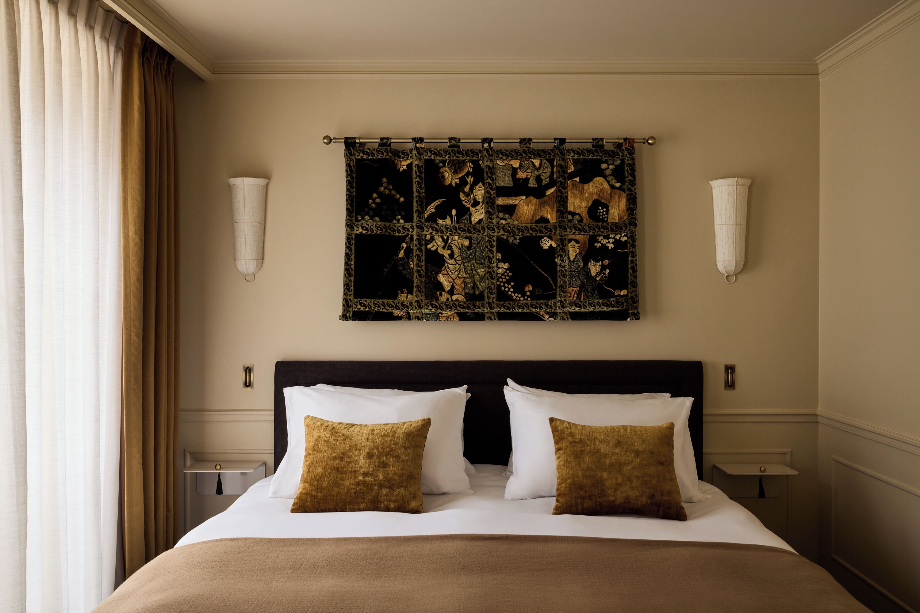 A hotel room with a large bed, two bedside tables, a headboard, and a decorative tapestry on the wall.