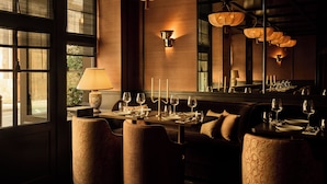 A dimly lit restaurant with a long table set for dining, cushioned seating, and a large mirror reflecting the interior. - L'Opale Noire (Paris)