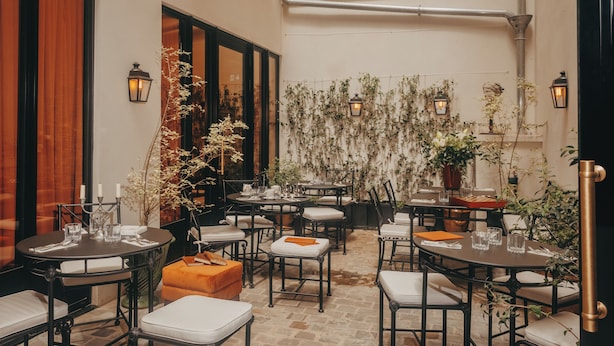 An outdoor dining area with tables and chairs, potted plants, and wall-mounted lanterns. - L'Opale Noire (Paris)