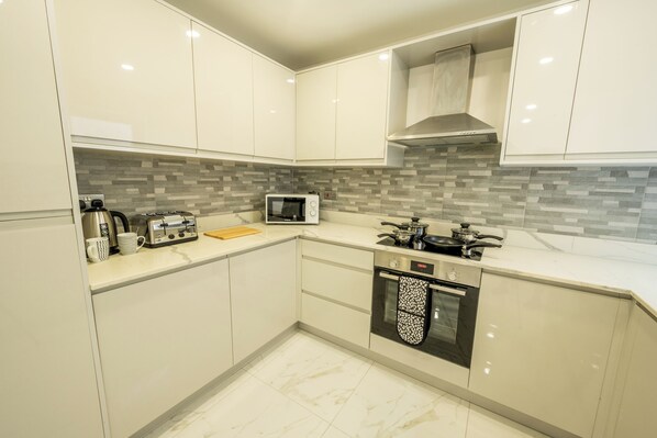 A modern kitchen with white cabinets, a microwave, a stove, and a tiled backsplash. - Eden Grove by Guestz (Appleby-in-Westmorland)