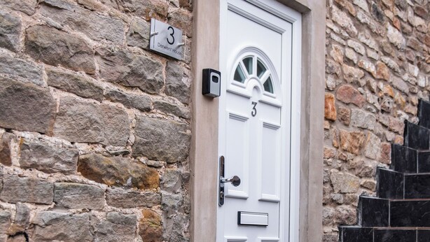 Une porte blanche portant le numéro 3, encastrée dans un mur de pierre, avec une petite boîte aux lettres au-dessus.