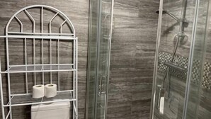 Una ducha con puerta de cristal, un estante metálico con toallas y una zona de ducha con azulejos.