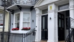 Un edificio con puerta negra, detalles blancos y barandilla de hierro negro.