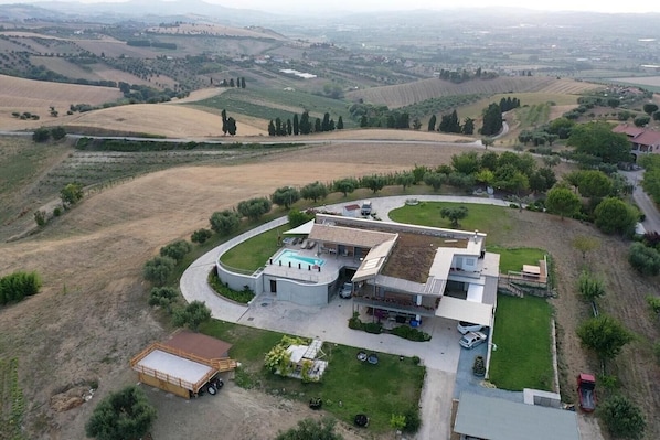 A modern house with a swimming pool, surrounded by rolling hills and vineyards.