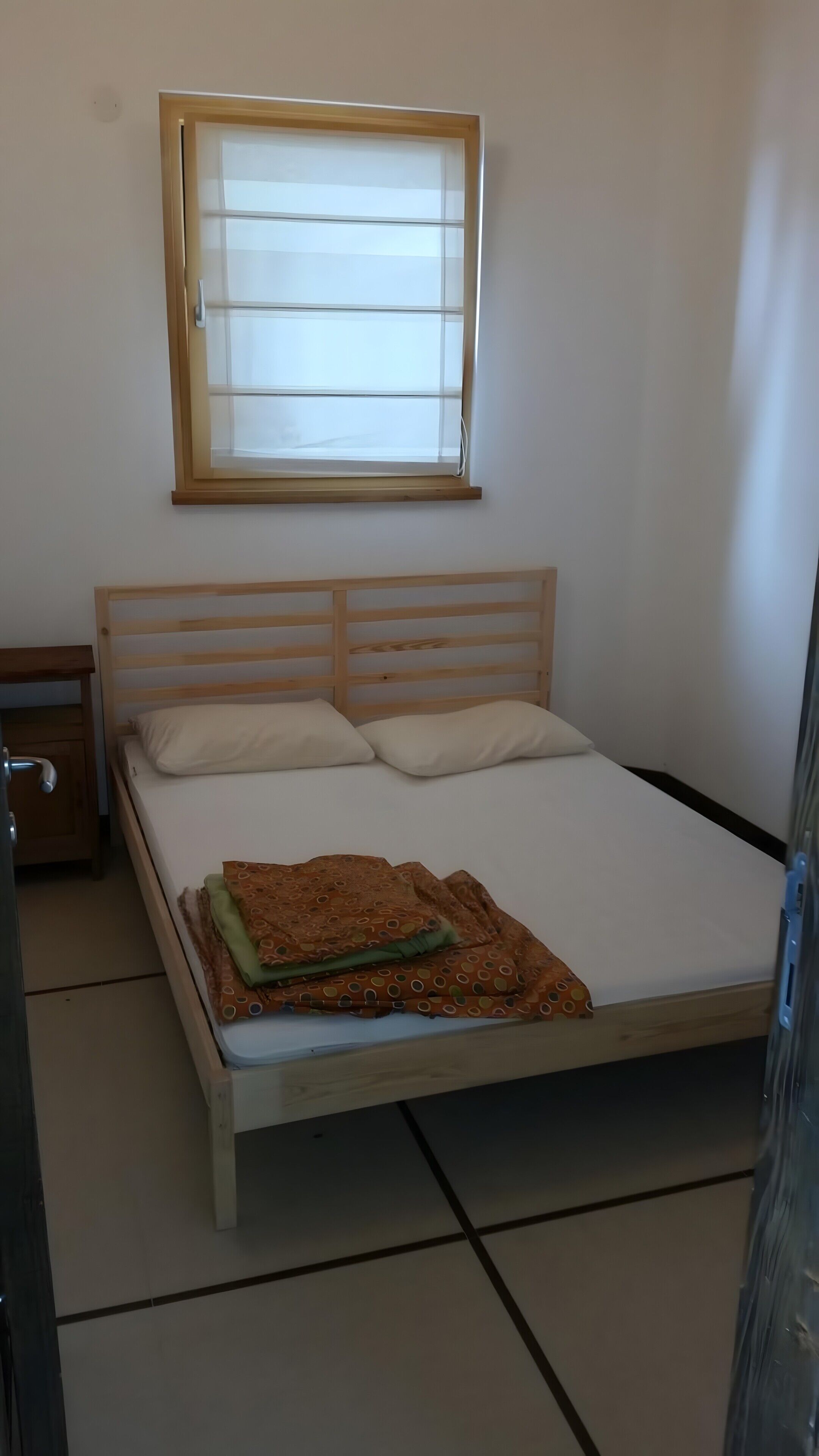A single bed with a wooden headboard, a window above it, and a nightstand to the left.