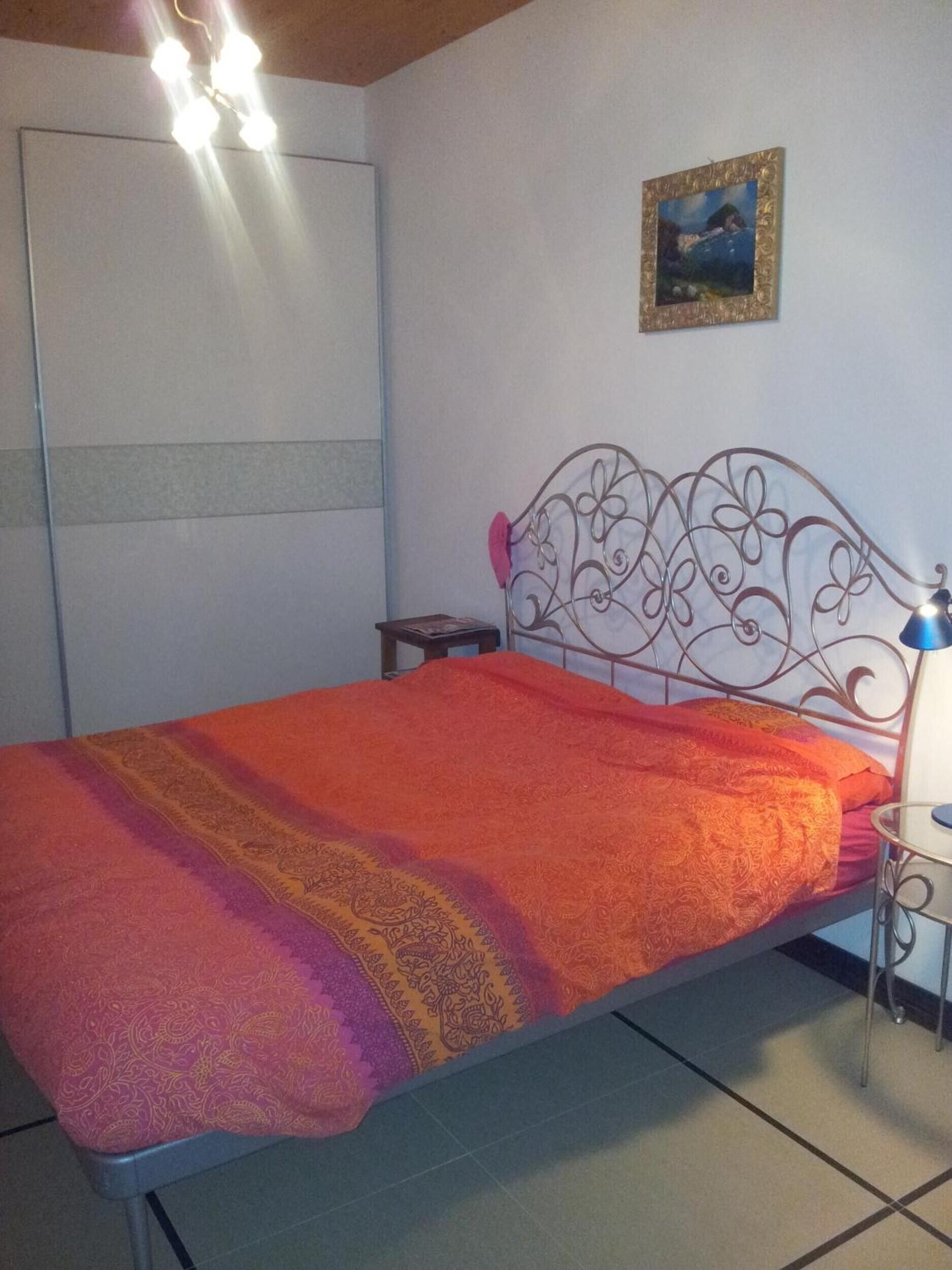 A bed with a metal headboard, a bedside table, a lamp, and a painting on the wall.