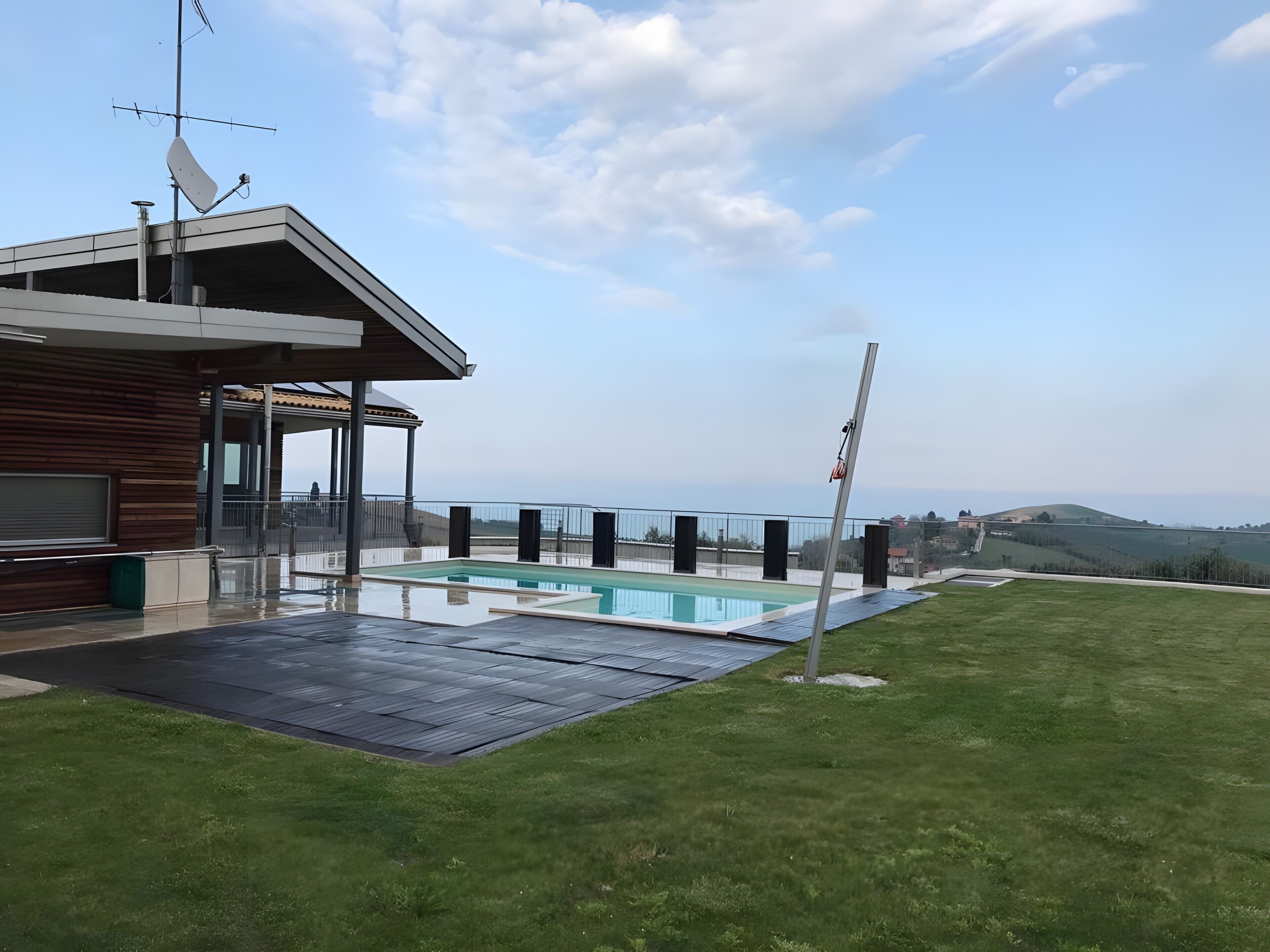 A modern house with a swimming pool, a covered patio, and a view of the countryside.