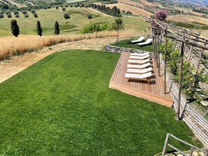 Eine grüne Holzterrasse mit Liegestühlen, mit Blick auf eine hügelige Landschaft mit Bäumen und Feldern.