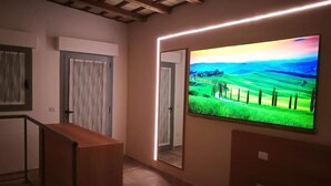 Un pasillo con un banco de madera, una puerta y un televisor grande de pared que muestra un paisaje.