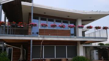 Un bâtiment moderne à deux étages, doté d’un balcon, d’un espace extérieur aménagé pour s’asseoir et de plantes en pot.