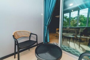 A balcony with a wicker chair, a black chair, and a dining table with chairs.