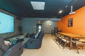 A modern living room with a large screen, a sofa, a dining table, and chairs. - Austin Shoplot Grand KTV Party 3BR 9Pax Mahjong Chill (Tebrau)