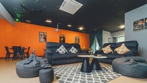 A modern living room with a black sofa, two bean bags, a patterned rug, and a ceiling light fixture. - Austin Shoplot Grand KTV Party 15pax Mahjong Chill (Tebrau)