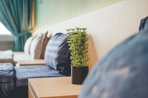 Una camera moderna con un comodino in legno, una pianta in vaso e un divano blu con cuscini a righe.