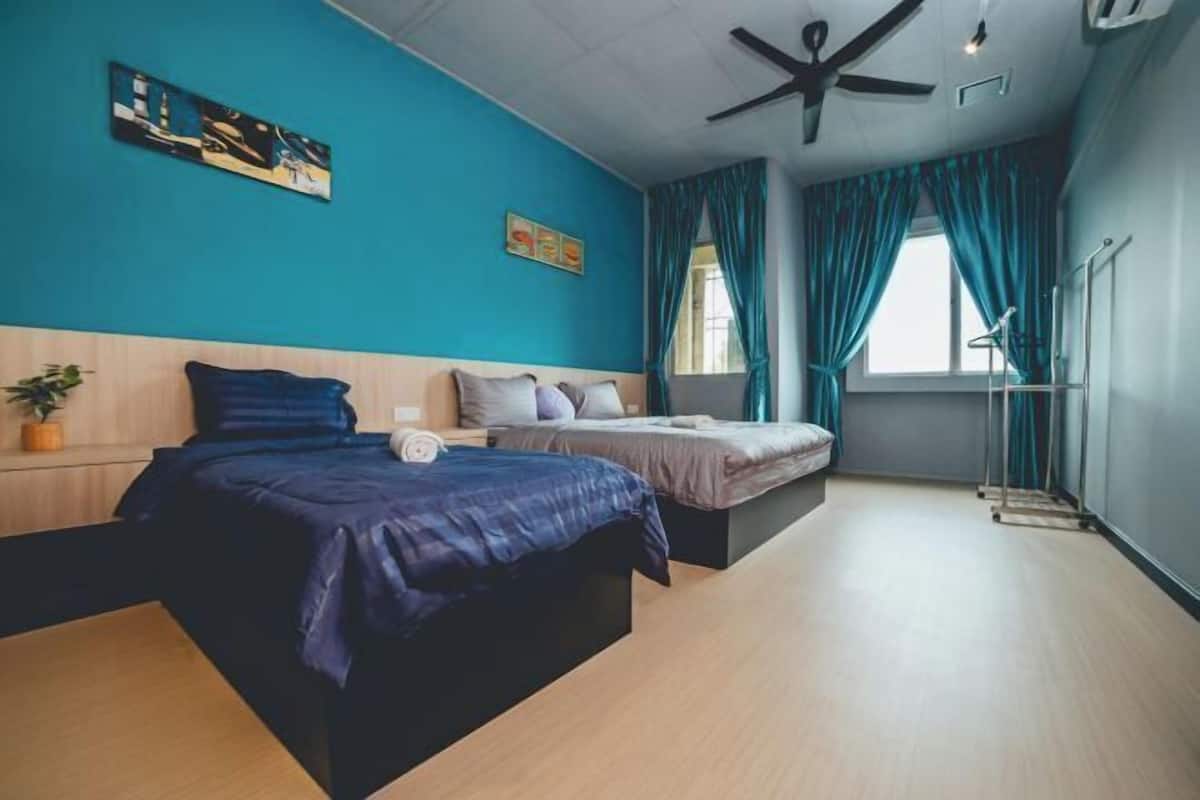 A room with two beds, a ceiling fan, a window with curtains, and a wall-mounted artwork.