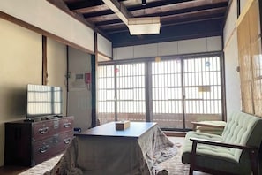 Una habitación japonesa tradicional con suelo de tatami, una mesa baja, un sofá y un televisor sobre un mueble.