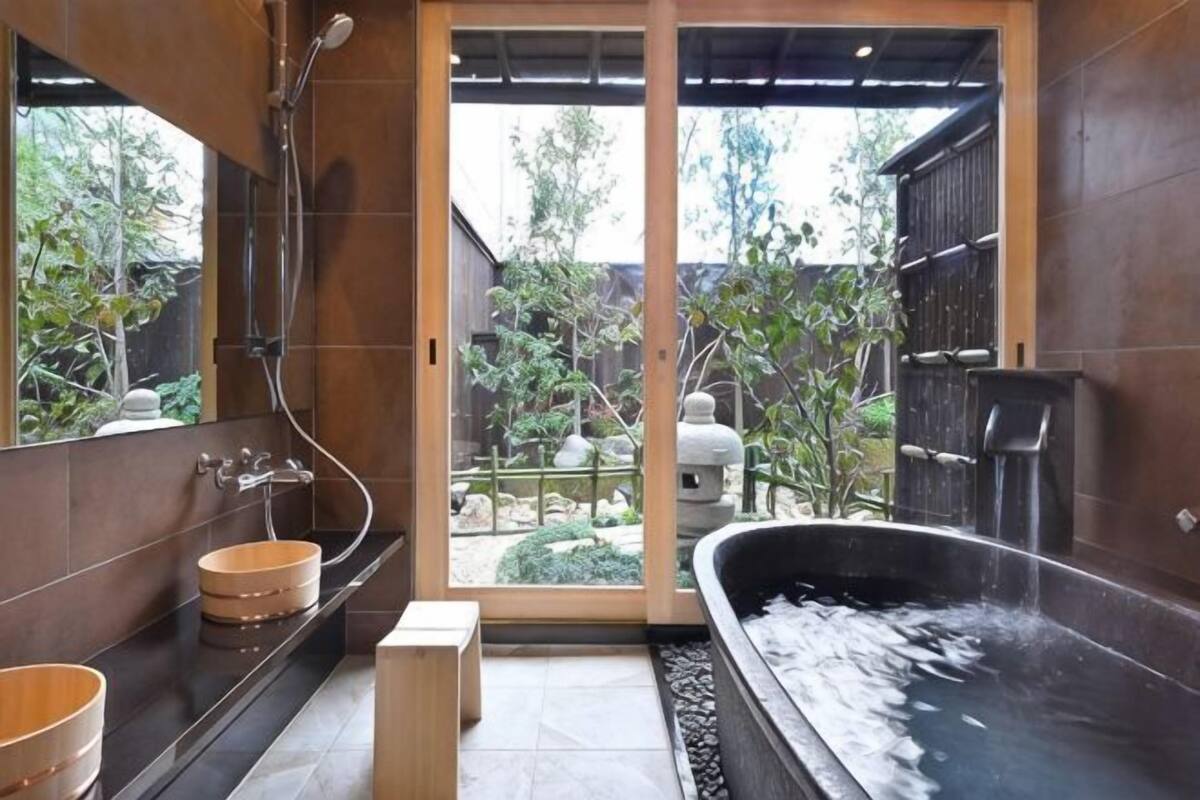 A bathroom with a bathtub, a wooden basin, a shower, and a view of a garden.