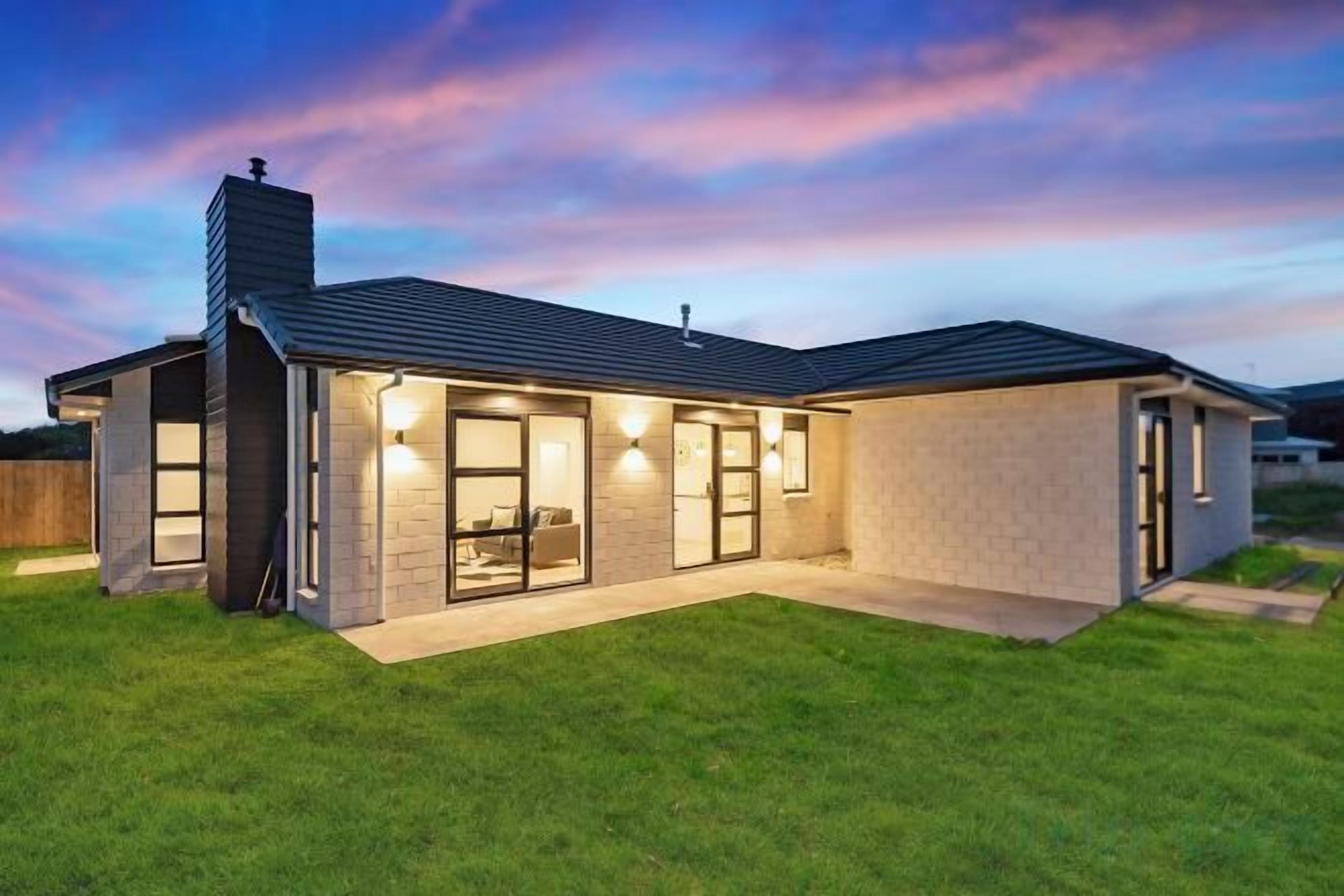 A modern house with a covered patio, a chimney, and a well-maintained lawn.