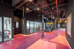 A gym with exercise equipment, a red floor, and a black wall with a logo. - Bliss Residence Old Klang Road by FEEL HOME (Kuala Lumpur)