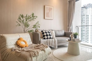 A living room with a sofa, armchair, and coffee table, a potted plant, and a city view. - Bliss Residence Old Klang Road by FEEL HOME (Kuala Lumpur)
